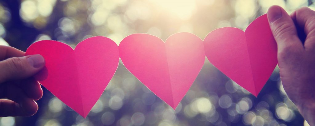 hands holding a string of paper hearts up to the sun